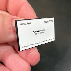 May include: A white business card with black text. The card reads "Pierce & Pierce, Merger and Acquisitions, Patrick Bateman, Vice President, 358 Exchange Place New York, N.Y. 10099, Fax 212 555 6990, Telex 41624", and has a phone number of "212 555 6342".