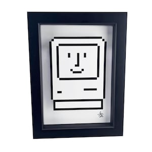 May include: A black framed print of a pixelated image of a vintage Macintosh computer with a smiling face. The print is signed "Josh 92".