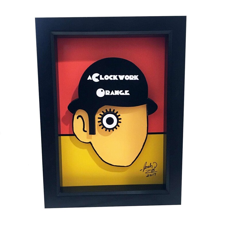 May include: A framed illustration of a character from the film "A Clockwork Orange". The character is wearing a black bowler hat and has a large, white eye. The title of the film is written in white letters on the hat. The illustration is set against a red and yellow background.