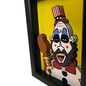 May include: A framed papercraft artwork of a cartoon character with a red, white, and blue hat, a red bow tie, and a white beard. The character is holding a brown and orange object in their right hand. The background is yellow.