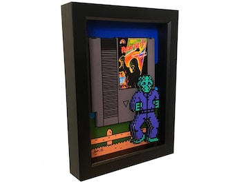 May include: A framed 3D pixel art piece featuring a character from the Friday the 13th video game. The character is standing in front of a NES game cartridge with the game's title "Friday the 13th" visible. The artwork is set against a blue background.