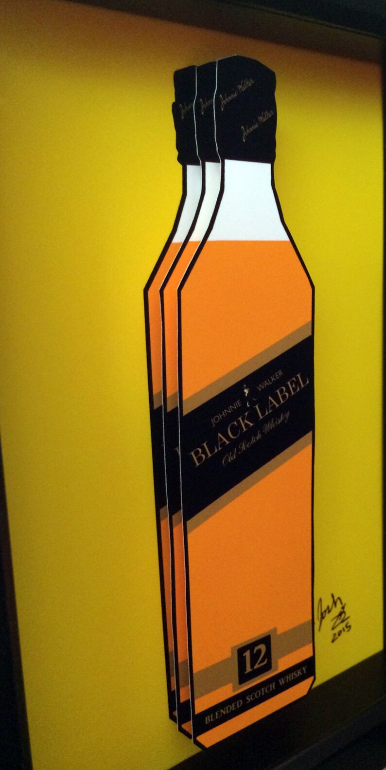 K&ouml;nnte beinhalten: Drei &uuml;bereinander gestapelte Papp-Ausschnitte von Johnnie Walker Black Label 12 Jahre altem Blended Scotch Whisky Flaschen. Die Flaschen sind orange und goldfarben mit schwarzem Text und einem Schwarzwei&szlig;bild eines Mannes, der geht. Der Text auf den Flaschen lautet "Johnnie Walker Black Label Old Scotch Whisky 12 Blended Scotch Whisky".