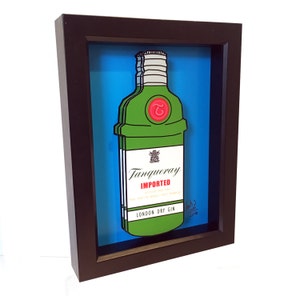 Puede incluir: Una ilustraci&oacute;n enmarcada de una botella de ginebra Tanqueray verde con una etiqueta roja y un sello de cera roja. La botella est&aacute; sobre un fondo azul. La obra de arte est&aacute; firmada y fechada.