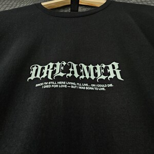 May include: Black crew neck sweatshirt with the word "DREAMER" in a gothic font. Below the word is the quote: "SINCE I'M STILL HERE LIVING, I'LL LIVE... OR I COULD DIE. I DIED FOR LOVE - BUT I WAS BORN TO LIVE."
