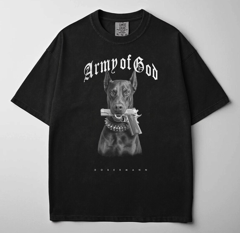 May include: Black t-shirt featuring a black and white graphic of a Doberman dog holding a gun in its mouth. The text "Army of God" is arched above the dog, with "Dobermann" below.