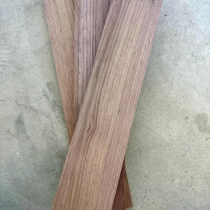 May include: A close-up shot of four rectangular wooden planks. The planks are various shades of brown, with visible wood grain patterns. The planks are arranged in a slightly overlapping manner, showcasing their natural texture and color variations.