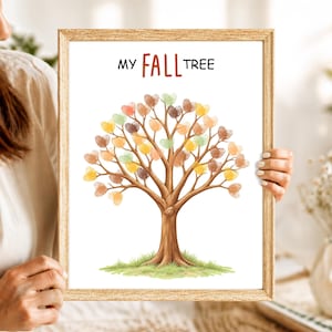 May include: A framed print titled MY FALL TREE featuring a brown tree trunk with green grass at the base. The branches are adorned with numerous small, heart-shaped thumbprints in various autumn colors including orange, yellow, and brown.