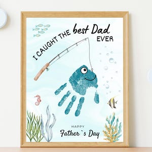 May include: A framed art print featuring a blue handprint transformed into a fish with a googly eye, hooked by a fishing rod illustration. The text reads I CAUGHT THE best Dad EVER and HAPPY Father's Day, surrounded by watercolor sea life.