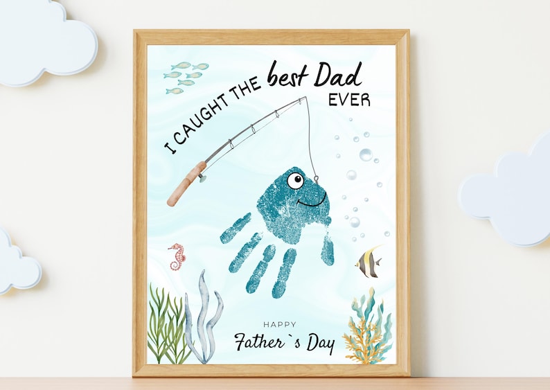 May include: A framed art print featuring a blue handprint transformed into a fish with a googly eye, hooked by a fishing rod illustration. The text reads I CAUGHT THE best Dad EVER and HAPPY Father's Day, surrounded by watercolor sea life.