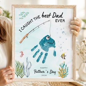 May include: A framed print featuring a blue handprint transformed into a fish on a fishing line. The text reads I CAUGHT THE best Dad EVER and HAPPY Father's Day 2026. The background includes illustrations of small fish, seaweed, and a seahorse.