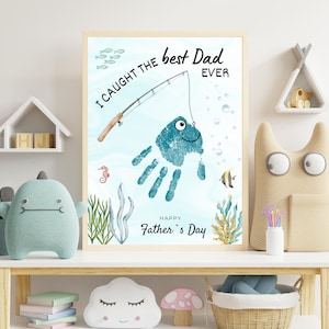 May include: A framed print featuring a teal handprint transformed into a fish with a fishing rod graphic. The text reads I CAUGHT THE best Dad EVER and HAPPY Father's Day. The background includes watercolor illustrations of seaweed, bubbles, and fish.