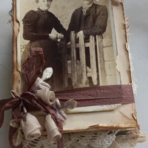 May include: A vintage photo of a couple is framed with brown ribbon and lace. The photo is decorated with brown and white fabric flowers.