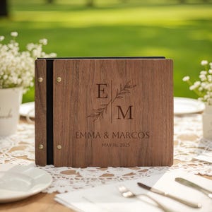 May include: A wooden wedding menu featuring the initials "E" and "M", the names "Emma & Marcos", and the date "May 16, 2025". The menu is displayed on a table set for a wedding reception, with cutlery and plates.