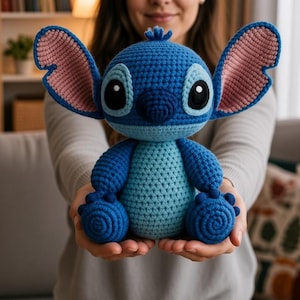 May include: A blue crochet plush toy featuring large ears with pink inner sections, a light blue belly, and dark blue limbs. The character has a round head, black eyes with white pupils, and a small tuft of hair on top, crafted with visible yarn stitches.