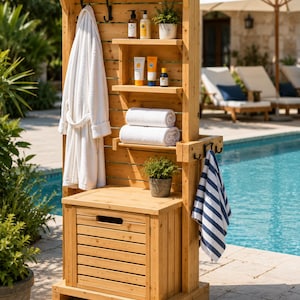 May include: A tall, light-brown wooden outdoor storage unit featuring a lower cabinet with a slatted door, two open shelves, and a vertical back panel with black metal hooks. It holds a white bathrobe, two white towels, toiletries, and a potted plant.