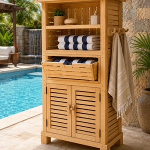 May include: A light brown wooden storage cabinet with slatted sides and doors. The unit features an open top shelf with a small plant and bottle, a middle shelf with folded navy and white striped towels, a pull-out drawer, and a lower cabinet.