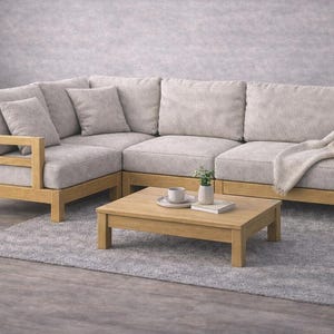 May include: A light gray sectional sofa with wooden frame and matching coffee table. The sofa has several throw pillows and a blanket draped over the arm. A small rug and a plant are in the scene.