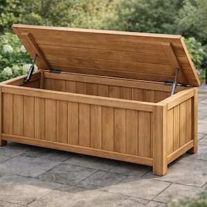 May include: A wooden outdoor storage chest with an open lid. The chest is made of light brown wood and has vertical paneling on the sides. The lid is propped open with metal hinges. The chest is sitting on a stone patio.