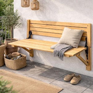 Puede incluir: Un banco plegable de madera clara está montado en una pared blanca. Una almohada beige y una manta gris descansan sobre el banco. Cestas de mimbre, una mesita y plantas decoran el espacio exterior. Un par de zapatos color canela están en el suelo.