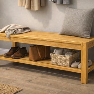 May include: A light-colored wooden bench with a lower shelf, holding shoes, a handbag, and a woven basket. A gray pillow and a folded blanket rest on top. The bench is in a well-lit room.