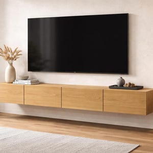 May include: A modern living room featuring a large black television mounted above a floating wooden cabinet. The cabinet has four doors and is made of light-colored wood. Decorative items include a vase with dried plants, books, and a tray with a decorative object.