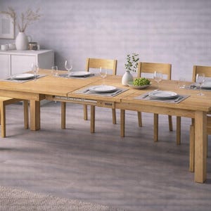 May include: A light-colored wooden dining table with six matching chairs. The table is set with plates, silverware, and wine glasses. A vase with greenery and a bowl of green grapes are on the table.