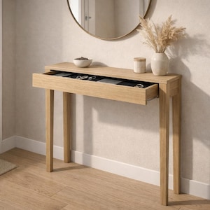 Puede incluir: Una consola de madera clara con un cajón abierto que revela joyas. Un espejo redondo cuelga sobre la mesa, y un jarrón con flores secas y un tarro pequeño están encima. La mesa está en una entrada bien iluminada.