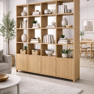 May include: A light oak wood bookcase with multiple cubby shelves and lower cabinets. The shelves are filled with books, plants, and decorative items. The bookcase is in a modern living room setting with a rug and a sofa.