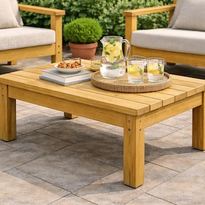 May include: A square wooden coffee table with a light brown finish, holding a tray with drinks and snacks. Two matching wooden armchairs with beige cushions are in the background. The table is 36 inches long and 36 inches wide.