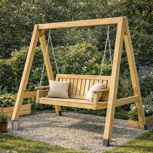 May include: A wooden swing set with a light brown finish, featuring a slatted bench and two beige pillows. The swing hangs from metal chains and is set on a gravel surface, surrounded by greenery. The frame is made of sturdy wooden beams.