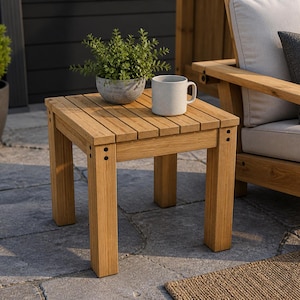 Puede incluir: Una pequeña mesa auxiliar cuadrada de madera clara con una parte superior de listones. Una pequeña maceta y una taza blanca están sobre la mesa. La mesa mide unos 46 cm cuadrados y tiene cuatro patas resistentes.