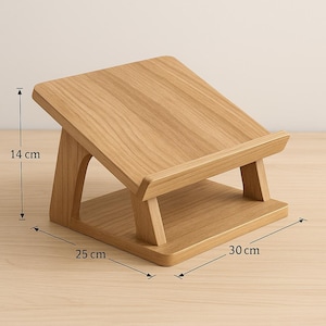 May include: A wooden laptop stand with a natural wood grain finish. The stand is 14 cm high, 25 cm wide, and 30 cm long. It features an angled top for comfortable viewing and a lower shelf for stability. The stand has a minimalist design.