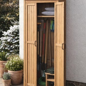 May include: A wooden outdoor storage cabinet with open doors, revealing gardening tools and accessories. The cabinet has a sloped roof and is made of light-colored wood. Inside are shovels, a rake, gloves, and a green hose. Two gray pillows rest on a shelf.