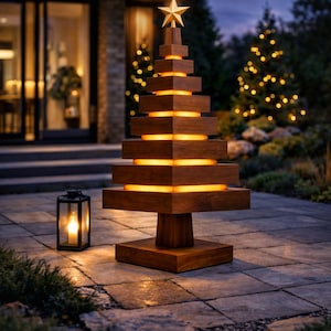 May include: A wooden Christmas tree sculpture with a gold star. The tree features a tiered design with warm, glowing lights between each layer. A black lantern with a lit candle is nearby, creating a festive outdoor scene.