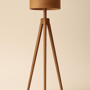 Op de afbeelding: Een houten vloerlamp met een statiefvoet en een cilindrische lampenkap. De lamp is gemaakt van lichtbruin hout en heeft een minimalistisch ontwerp. De lampenkap heeft een diameter van ongeveer 30 cm.