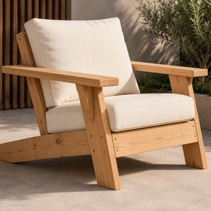Può includere: Una poltrona da esterno in legno con cuscino e schienale color crema. La sedia è realizzata in legno chiaro e presenta un design semplice e moderno. I cuscini sono di colore neutro e la sedia è posizionata su una superficie di cemento.