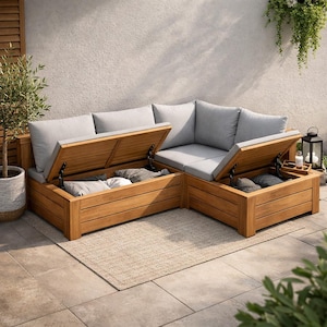 Puede incluir: Sofá seccional de exterior en forma de L con cojines de color gris claro y compartimentos de almacenamiento de madera. El marco de madera tiene un acabado natural. Los compartimentos de almacenamiento están abiertos, revelando almohadas. El sofá está sobre una alfombra de color neutro en un patio embaldosado.