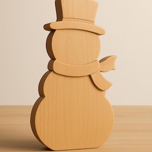 Peut inclure: Une figurine de bonhomme de neige en bois avec un chapeau haut de forme et une écharpe. Le bonhomme de neige est sculpté dans du bois de couleur claire et se dresse sur une surface en bois. C'est un objet décoratif.