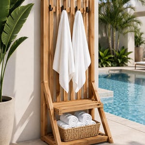 May include: A wooden towel rack with two white towels hanging from black hooks. The rack has a shelf with a woven basket holding rolled white towels. The rack is next to a pool.