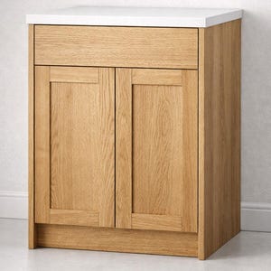 Puede incluir: Un mueble de baño de roble claro con encimera blanca. El mueble tiene dos puertas, un cajón y una base. La veta de la madera es visible en las puertas, el cajón y los laterales. La encimera es de color blanco liso.