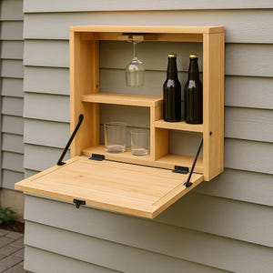 Op de afbeelding: Een lichtgekleurde houten buitenbarkast met een open deur. De kast heeft planken voor glazen en flessen, met een wijnglas ondersteboven. Twee flessen en twee glazen zijn zichtbaar.