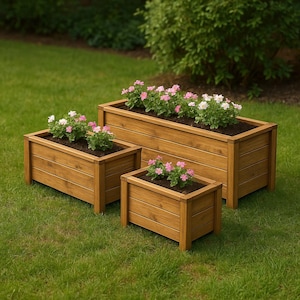 May include: Three wooden rectangular planters of varying sizes, filled with soil and blooming pink and white flowers. The planters are made of light brown wood and sit on a green lawn.