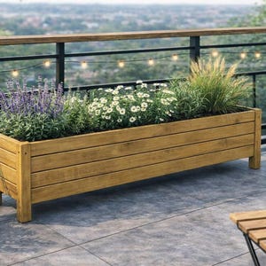 May include: A rectangular wooden planter box filled with various plants and flowers. The planter is made of light brown wood and sits on a patio. The plants include purple, white, and green foliage. The background features a railing and a view of the city.