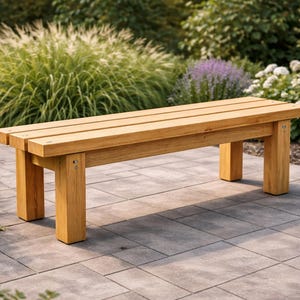 May include: A wooden outdoor bench with a natural finish. The bench has a slatted seat and four sturdy legs. It is set on a stone patio, surrounded by lush greenery and flowers, creating a serene outdoor setting.
