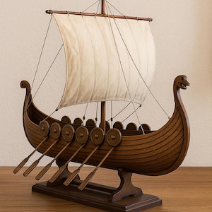May include: A detailed wooden Viking ship model with a cream-colored sail, oars, and shields. The ship features a curved hull, a mast, and a decorative dragon head at the bow. The model is displayed on a wooden stand.