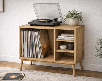 May include: A wooden record player stand with a black turntable on top. The stand has open shelving with vinyl records, books, and decorative items. A small potted plant sits on top. The stand is made of light-colored wood.