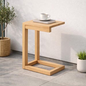 May include: A light-colored wooden side table with a C-shaped design. A white teacup and saucer sit atop a small book on the table's surface. The table is 24 inches tall.