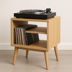 Puede incluir: Un tocadiscos negro se encuentra sobre un mueble de discos de color madera clara con dos estantes. Los discos de vinilo se guardan en el estante inferior. El mueble tiene patas anguladas y un diseño minimalista.