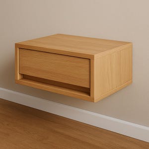 Puede incluir: Una mesita de noche flotante de madera clara con un solo cajón. La mesita es rectangular y está montada en una pared beige. El cajón está ligeramente empotrado y se aprecia la veta de la madera.