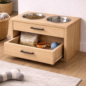Könnte beinhalten: Hölzerne Futterstation für Haustiere mit zwei Edelstahlnäpfen. Das Gerät hat eine Schublade mit einer Tüte Tierfutter, einem Halsband und einem blauen Ball. Das Gerät steht auf einem hellen Teppich.